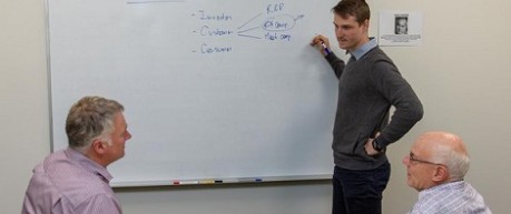 photo of three men in a meeting with writing on a white board - credit AbacusBio